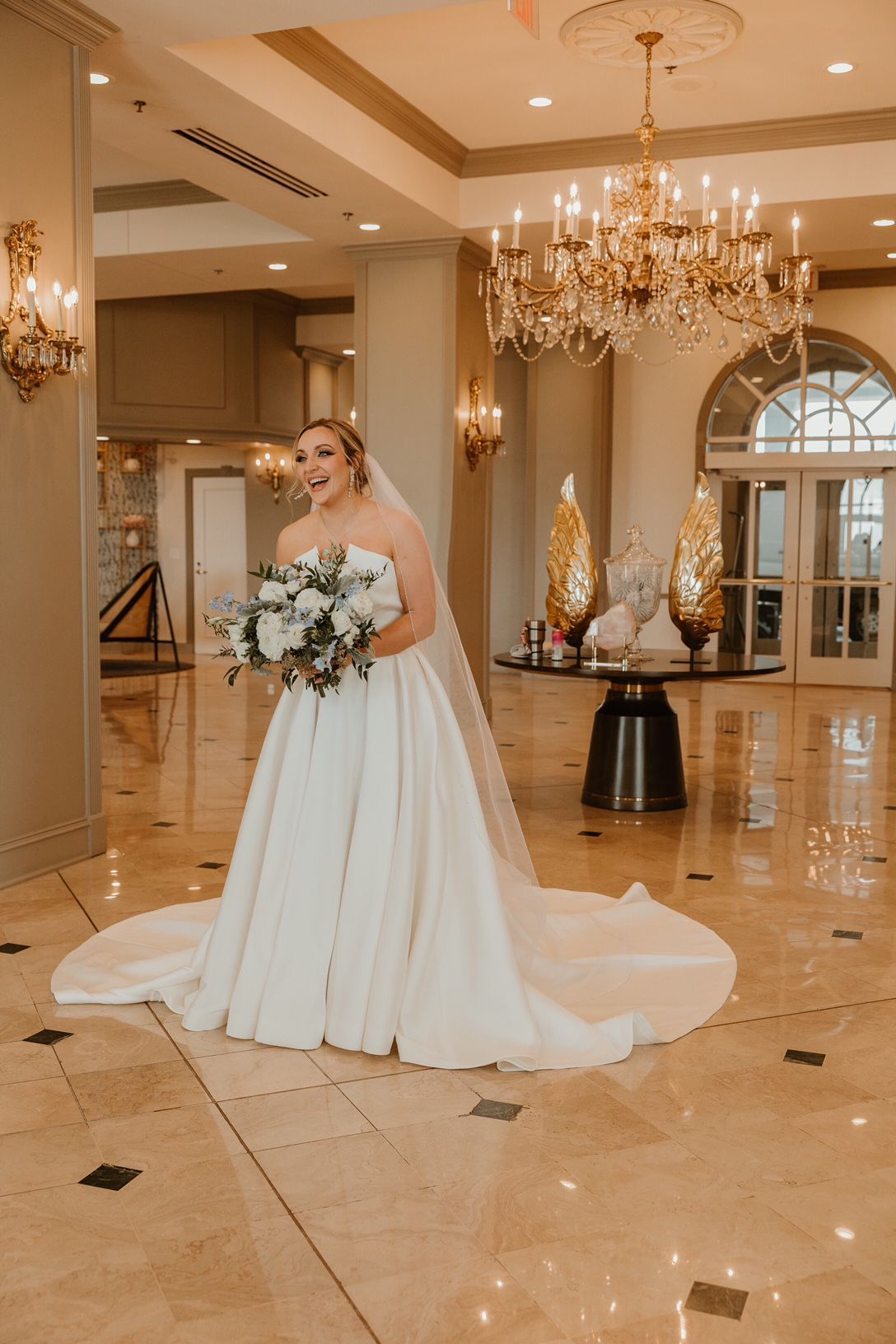 A bride in a wedding dress is standing in a hallway holding a bouquet of flowers.