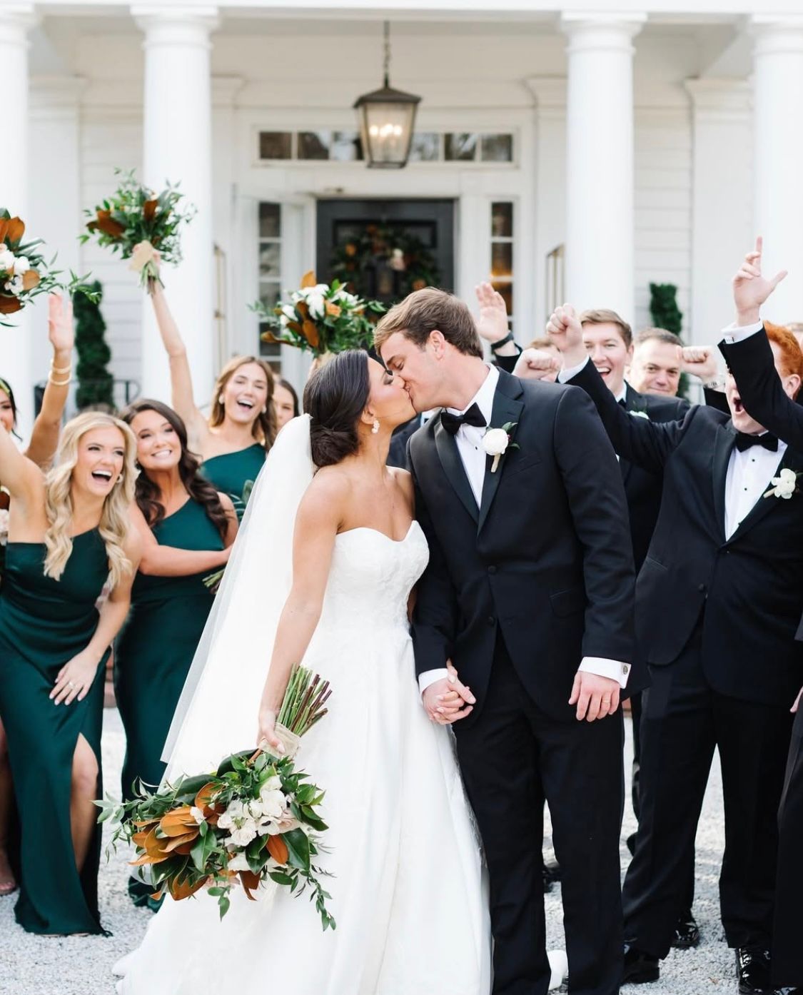 A bride and groom are kissing in front of their wedding party.
