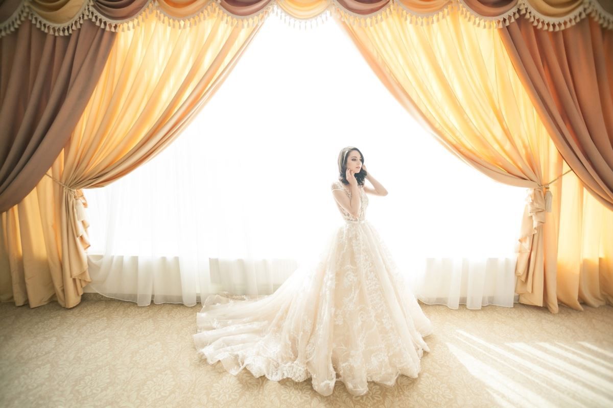 A woman in a wedding dress is standing in front of a window.