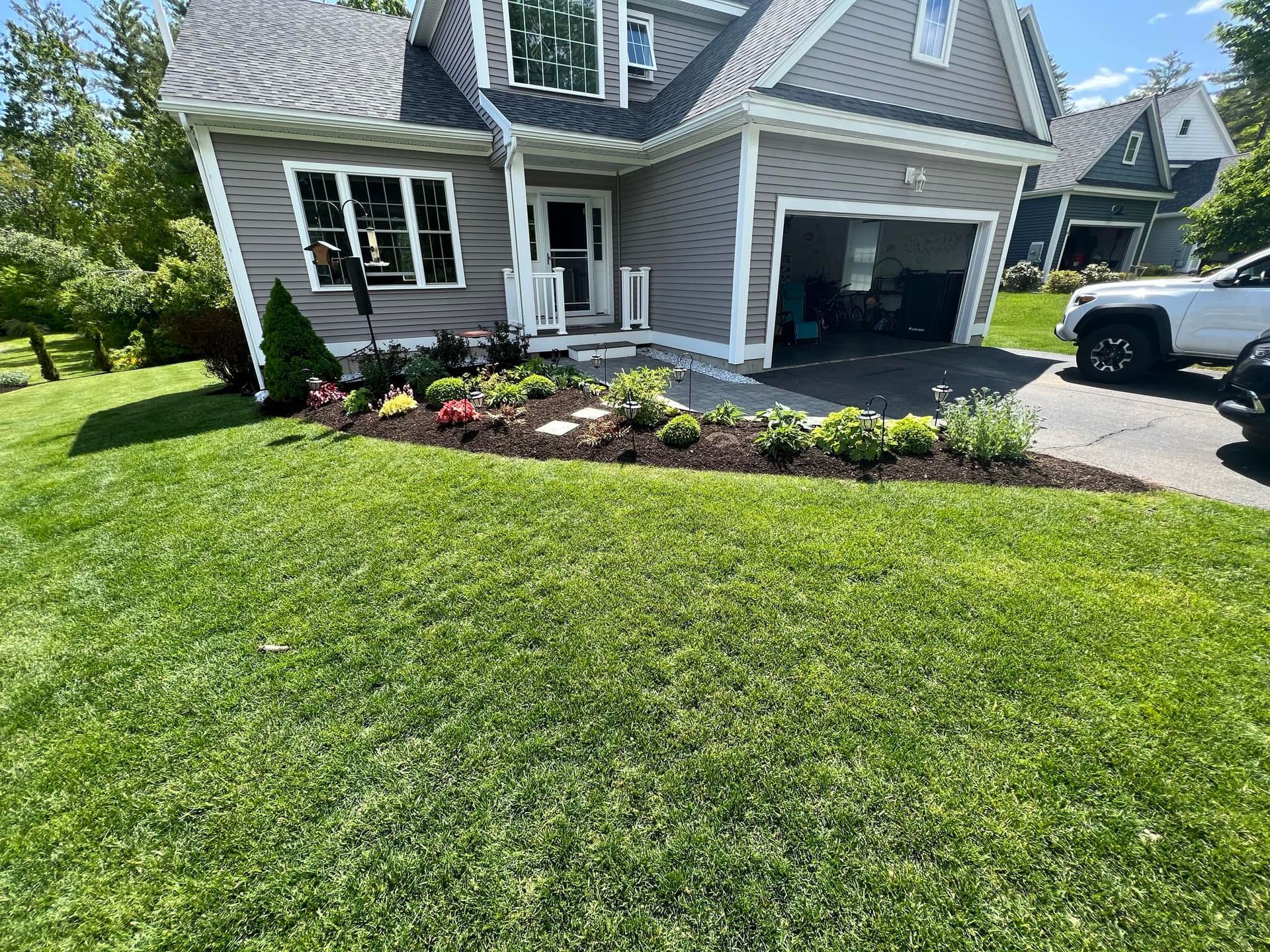 A house with a landscaped garden bed and a garage, sunny day.