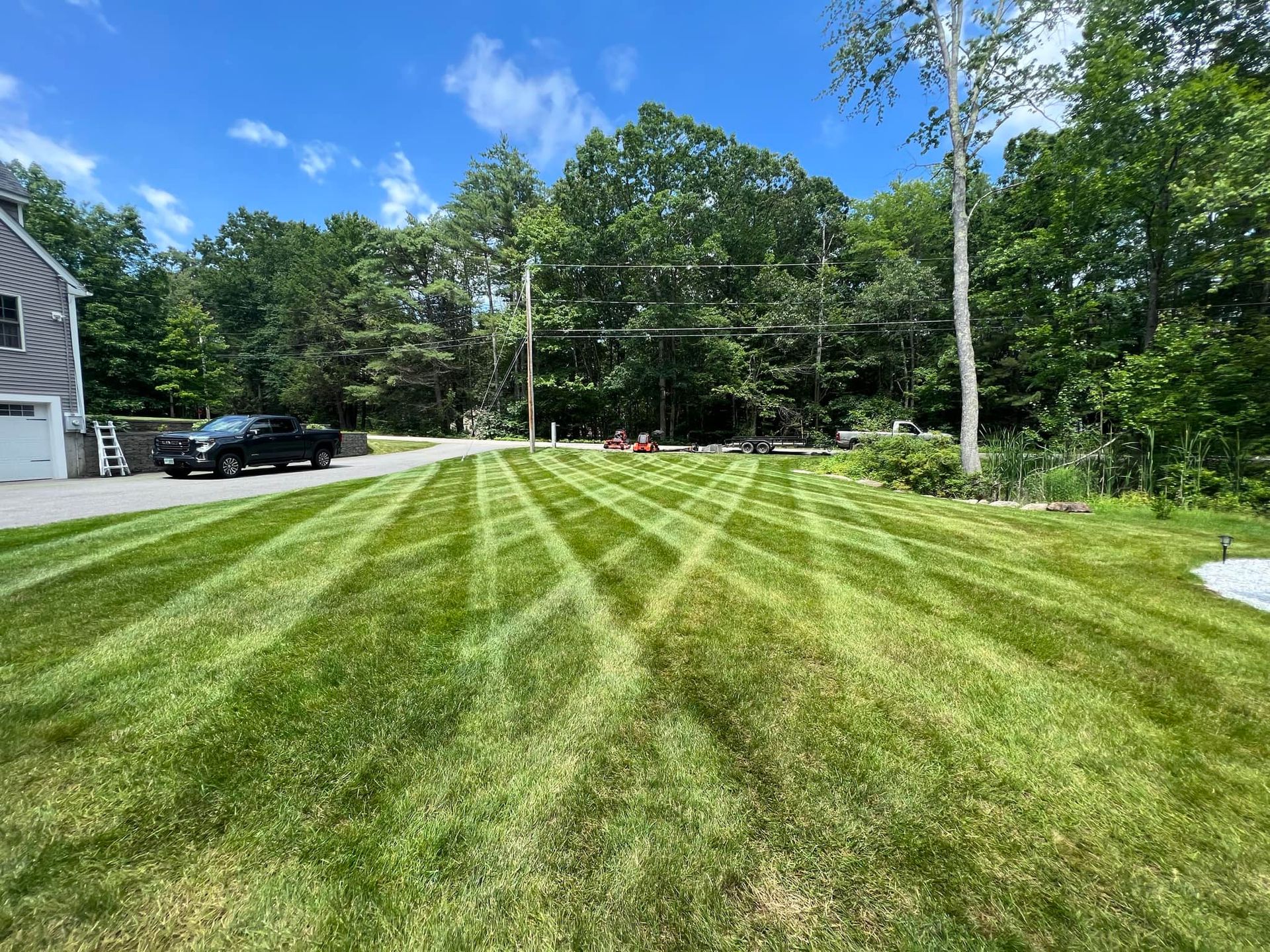 Lawn with geometric mowing pattern, black truck in driveway, trees, and bright blue sky.