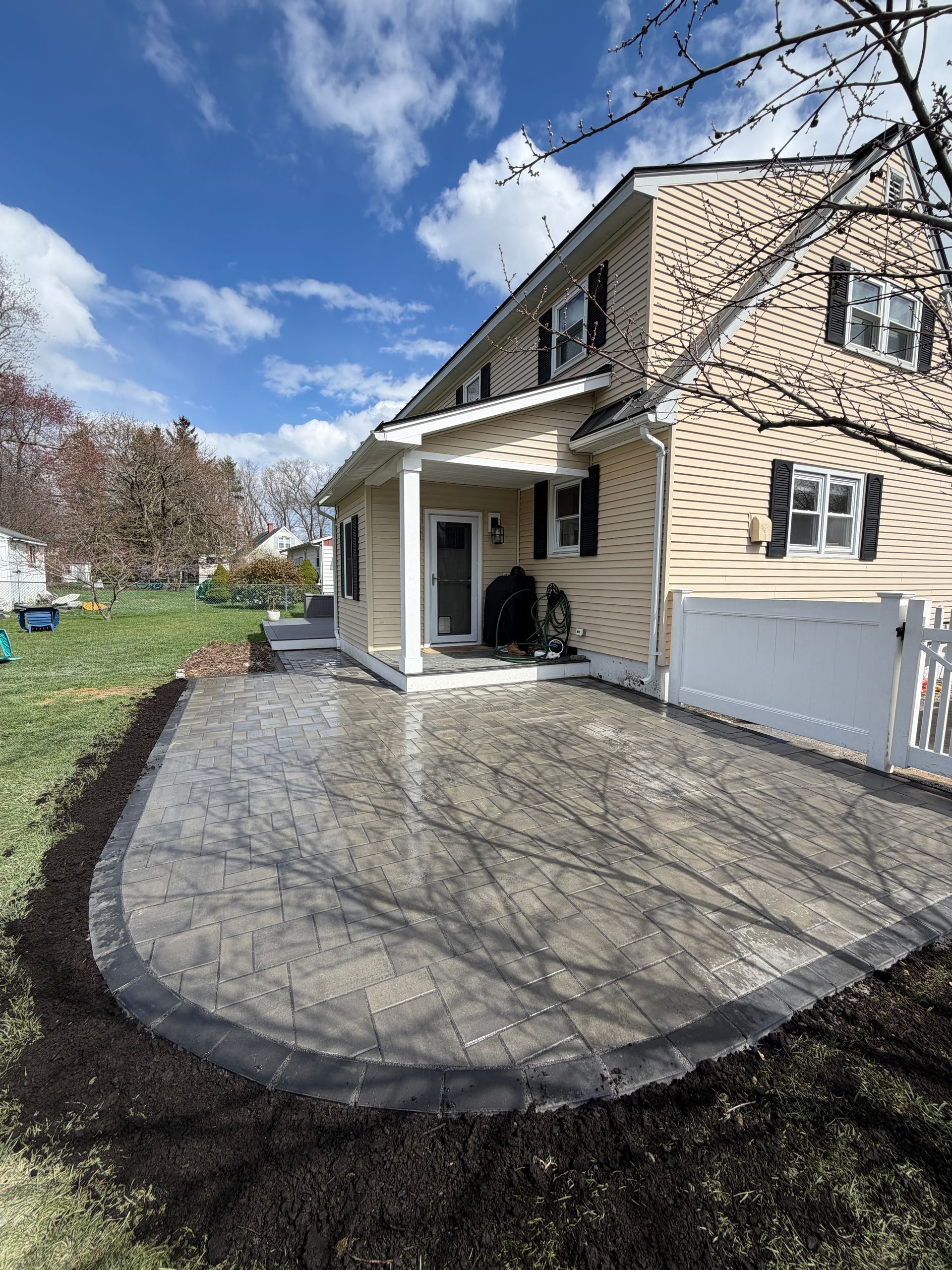 Front porch and curved patio of a beige house with white railings on a sunny day. 