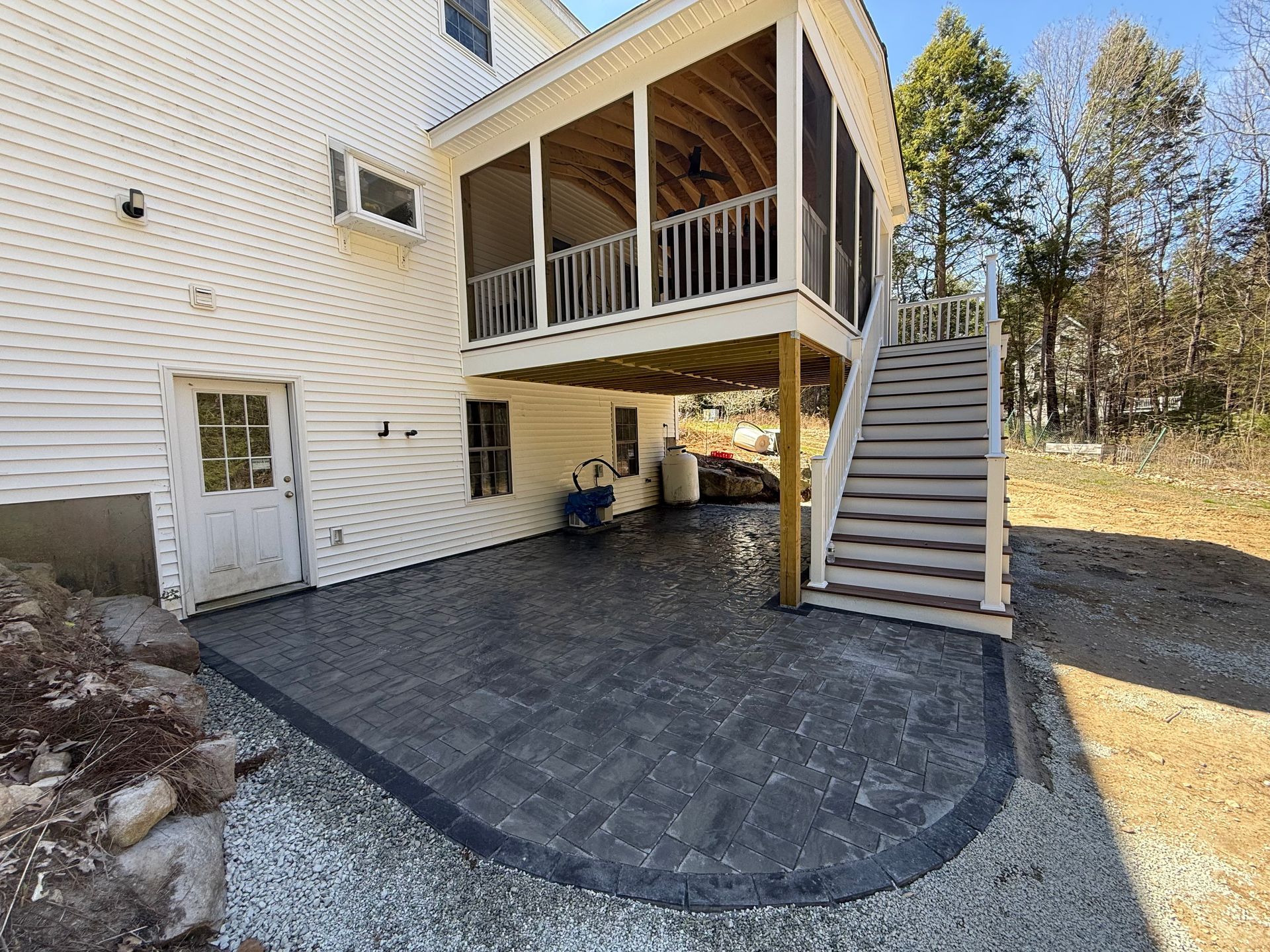 Raised back patio with stairs and covered deck beside a house, with a paved patio below. 