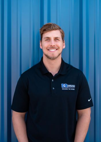 A man in a black polo shirt is standing in front of a blue wall.