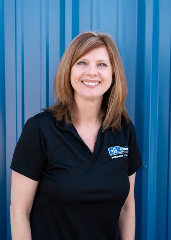 A woman in a black shirt is smiling in front of a blue wall.