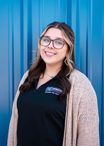 A woman wearing glasses and a sweater is smiling in front of a blue wall.