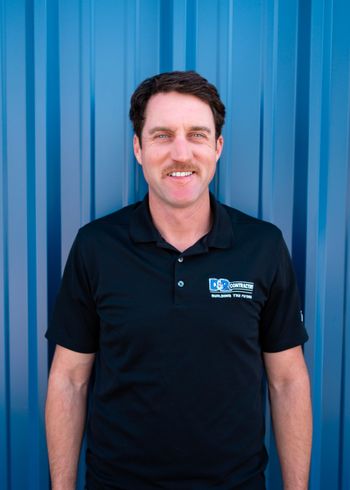 A man in a black shirt is standing in front of a blue wall.