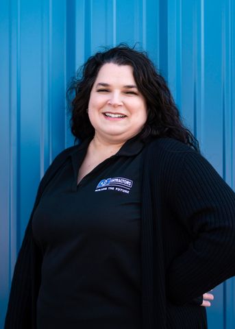 A woman in a black shirt and cardigan is standing in front of a blue wall.