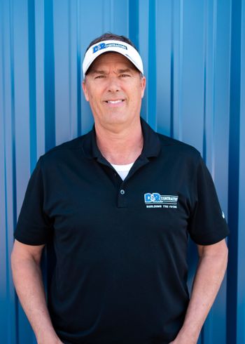 A man wearing a hat and a black shirt is standing in front of a blue wall.