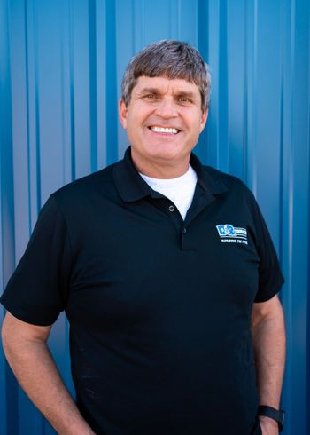 A man in a black shirt is standing in front of a blue wall.