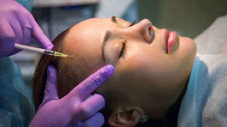 A woman is getting a botox injection in her forehead.