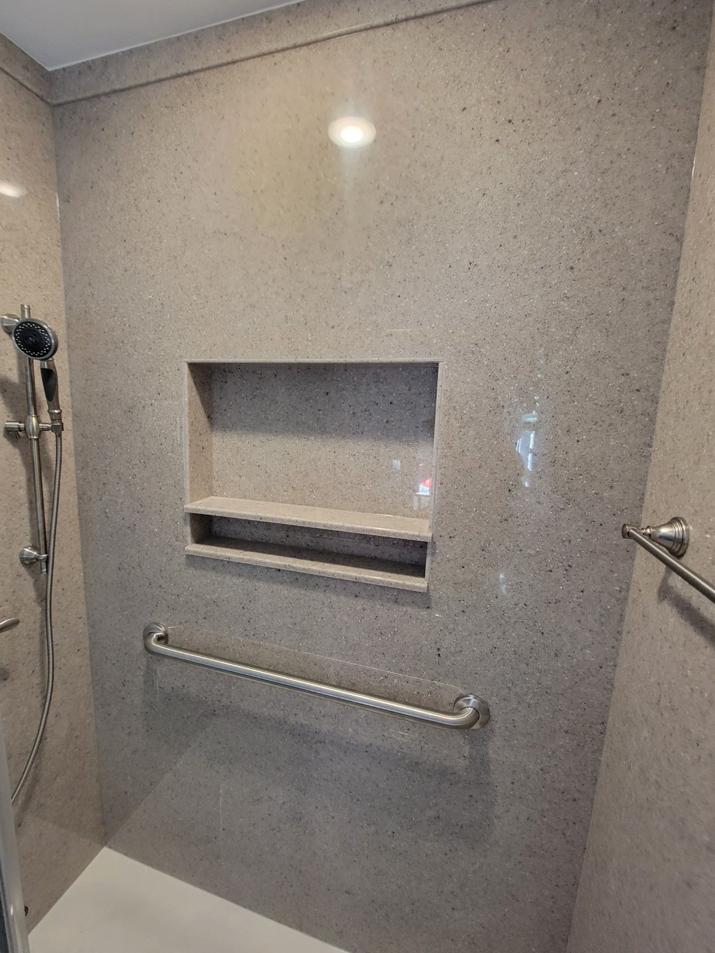 A bathroom with a walk in shower with a shelf and a hand rail.