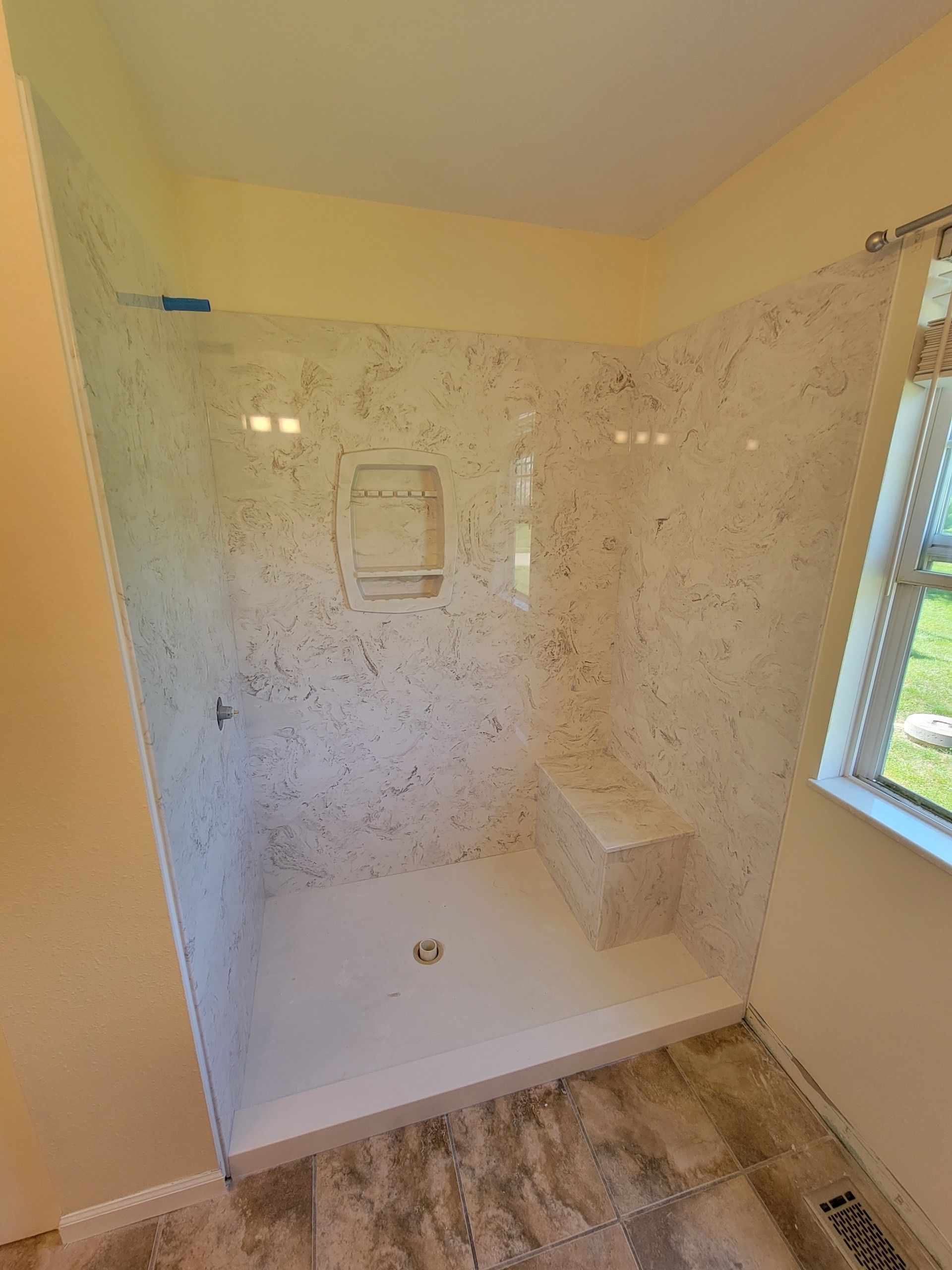 A bathroom with a walk in shower and a window.