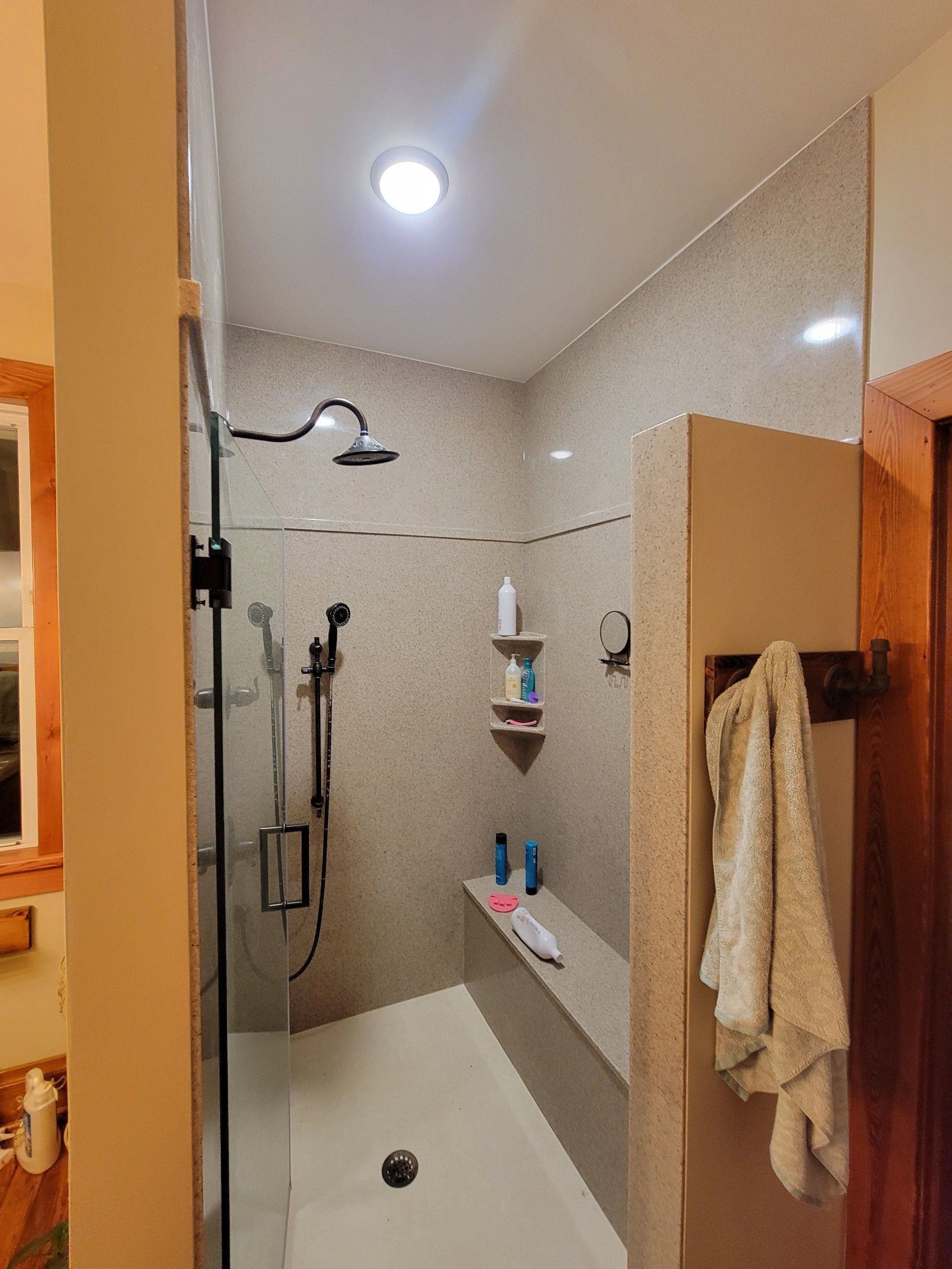 A shower with a corner seat and a drain in a bathroom.