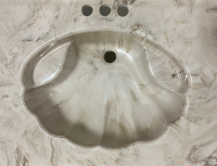 A bathroom sink in the shape of a shell on a marble counter top.