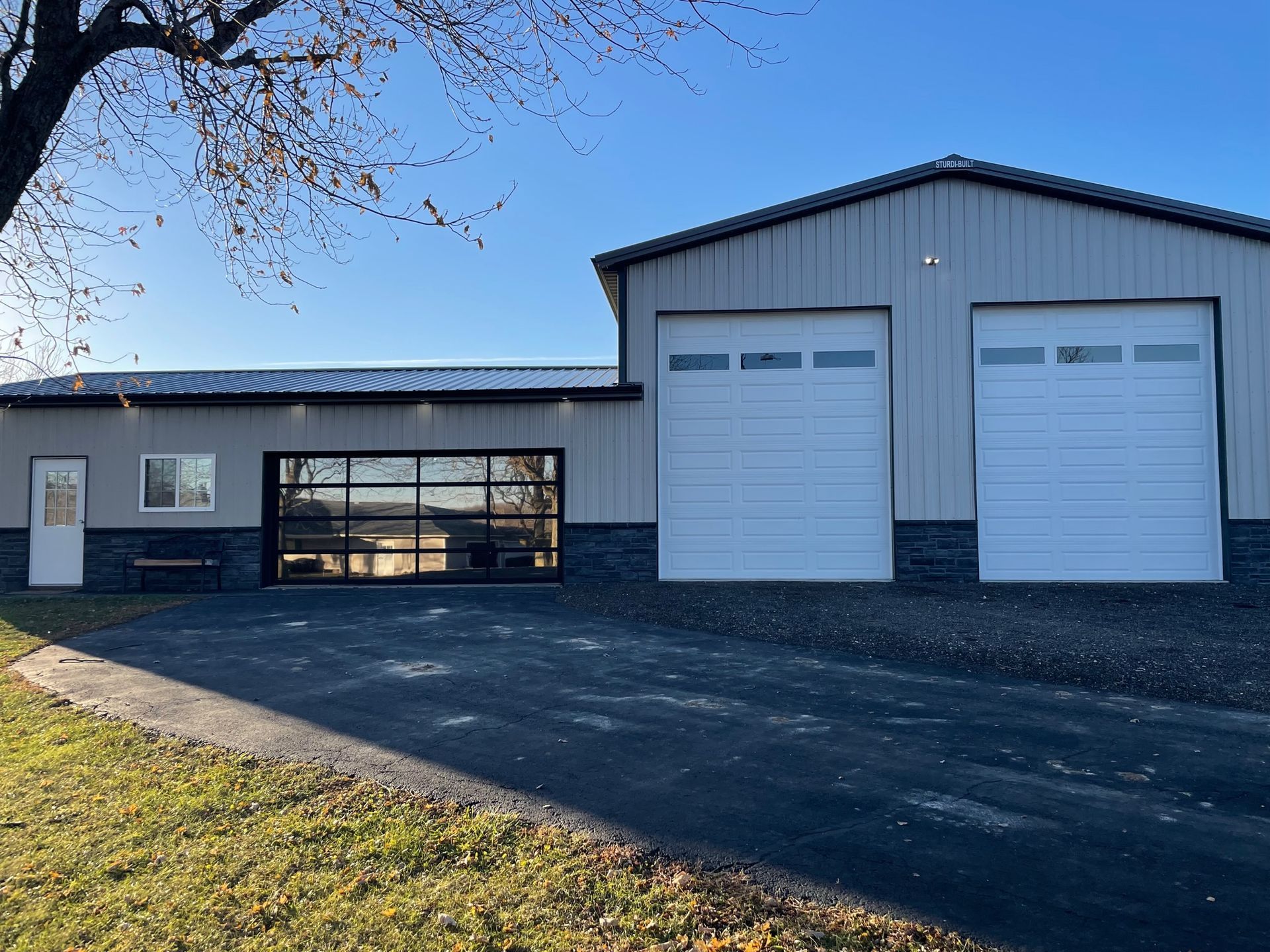 A large building with three garage doors and a tree in front of it.