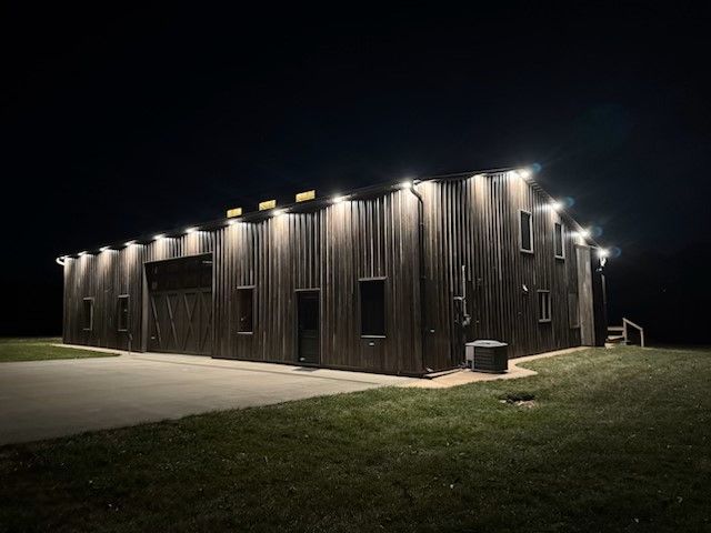 A large barn is lit up at night with lots of lights on the side.