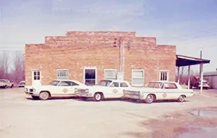 Three white cars are parked in front of a brick building.