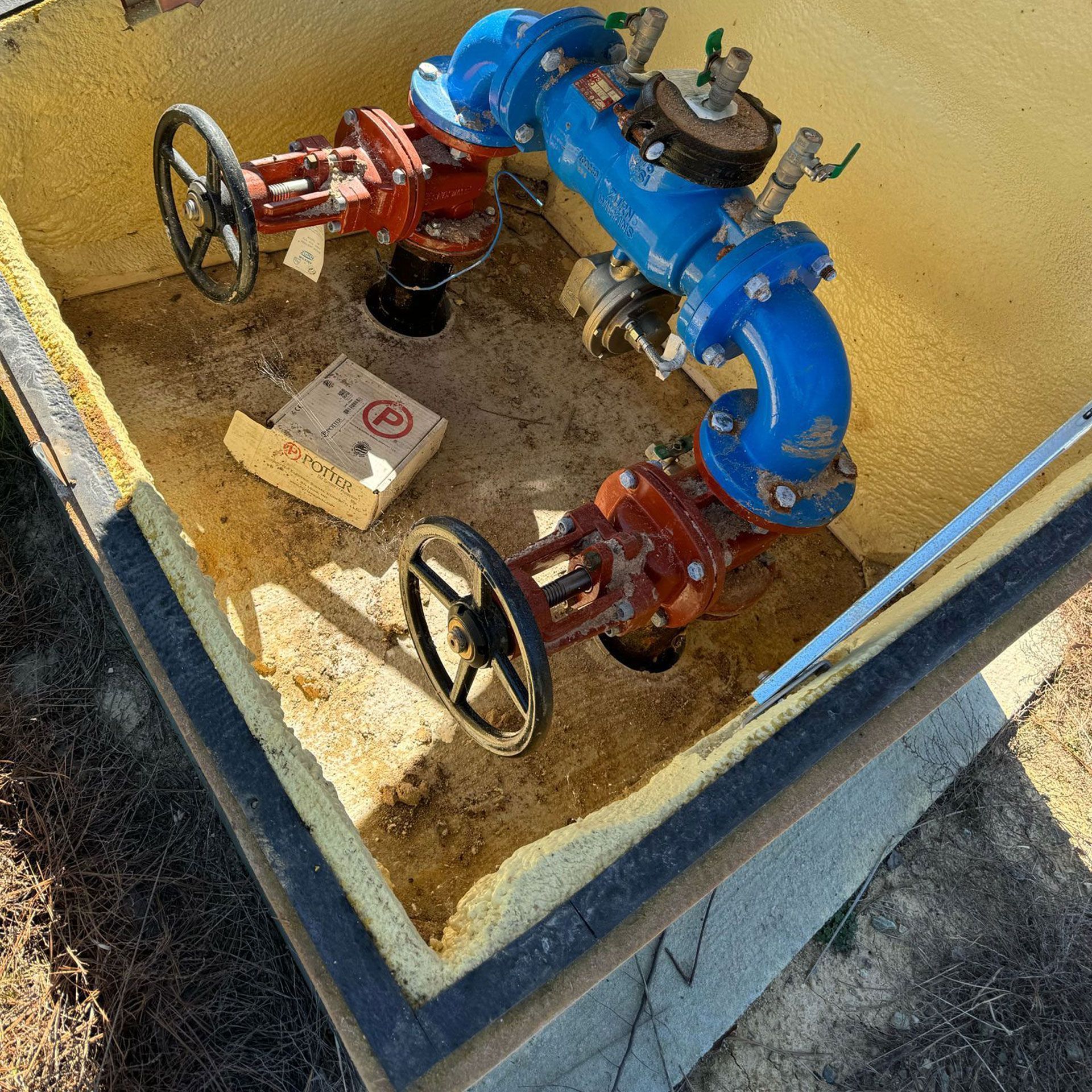 Blue and red water valves inside a rectangular, insulated concrete box with a lid.