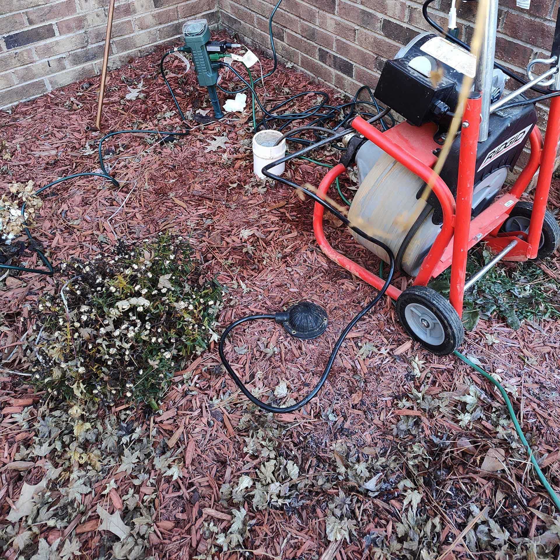 Red sewer cleaning machine, garden bed with mulch, and outdoor electrical setup.