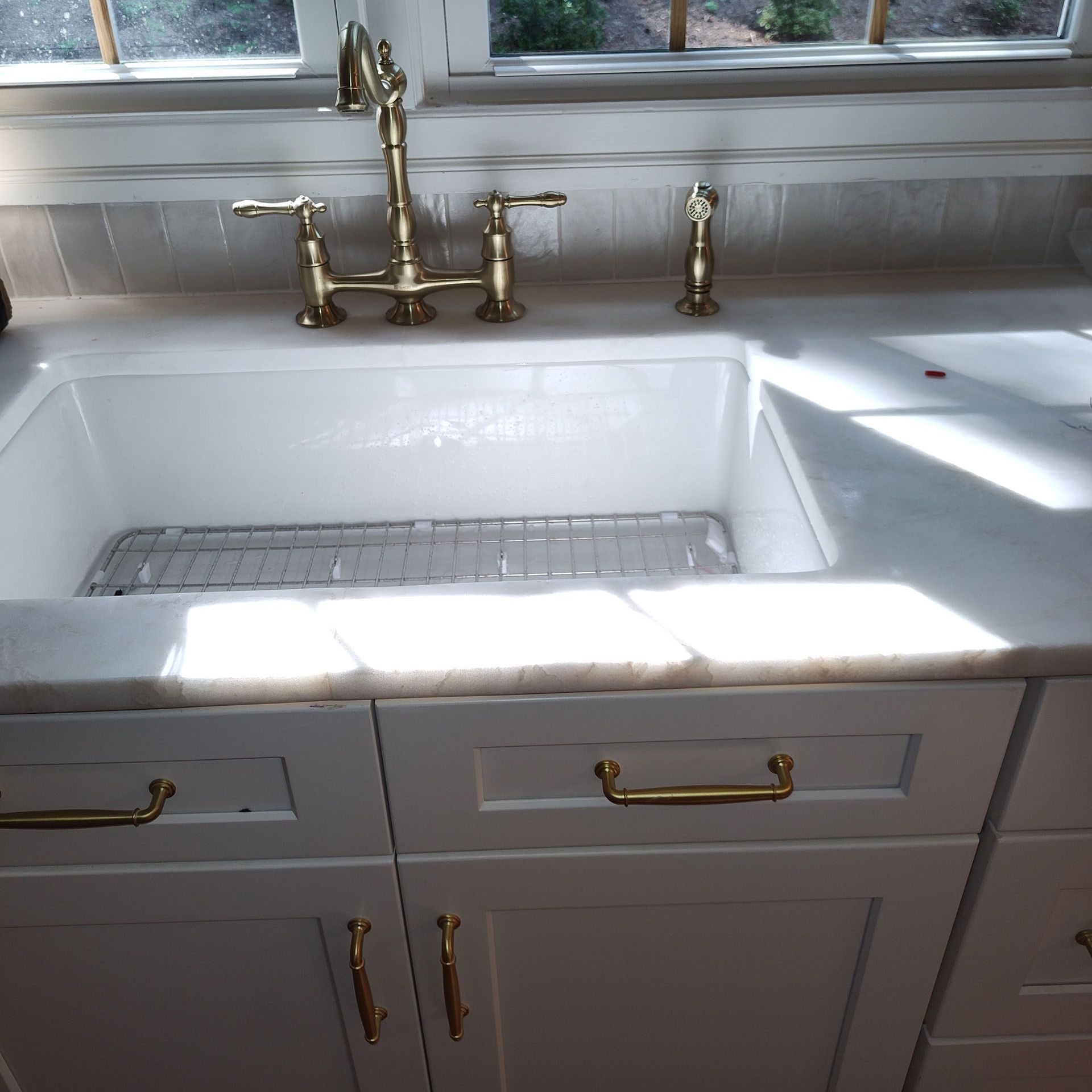 White farmhouse kitchen sink with brass faucet and hardware. White cabinets with gold handles.