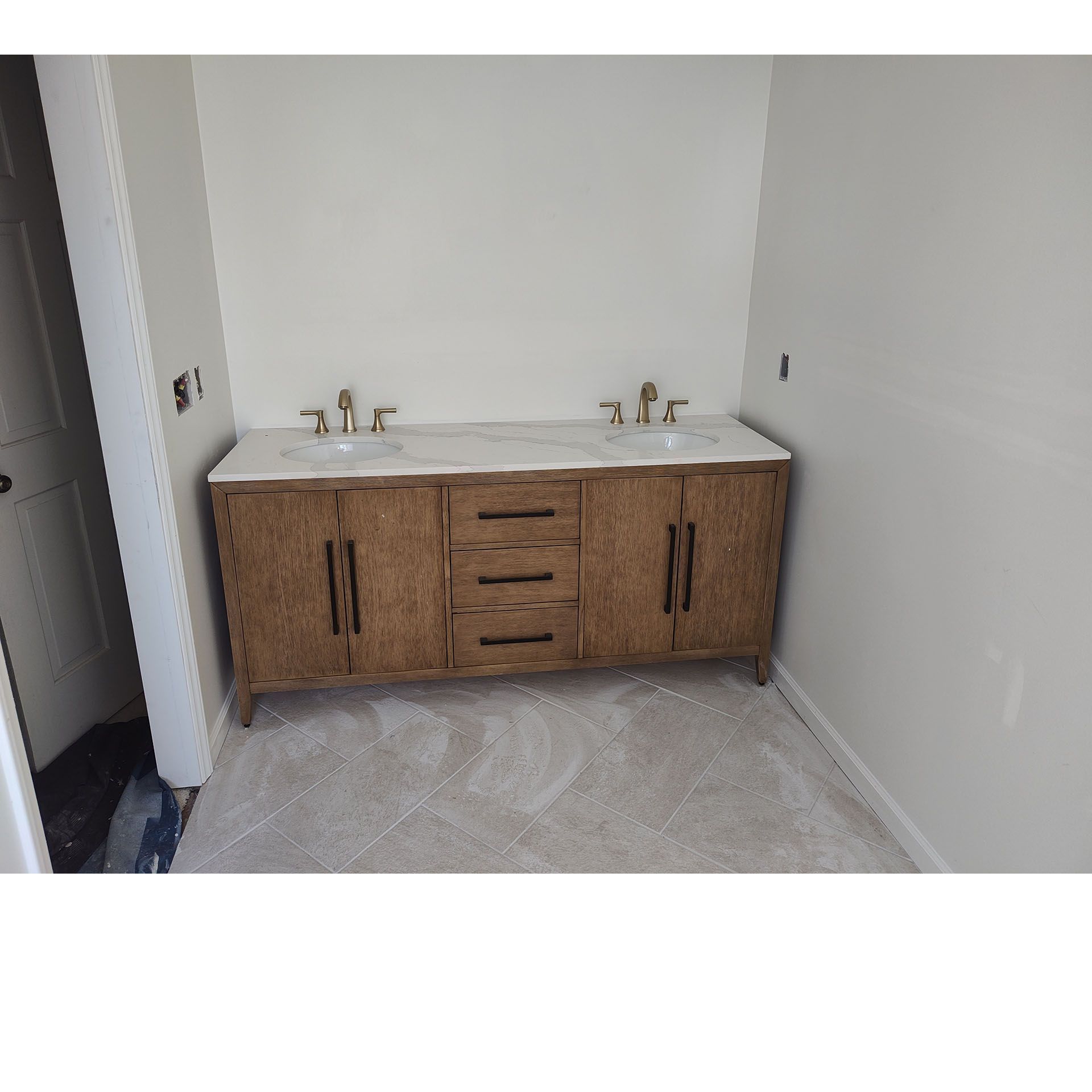 A wooden bathroom vanity with two sinks and gold faucets is placed against a light-colored wall.
