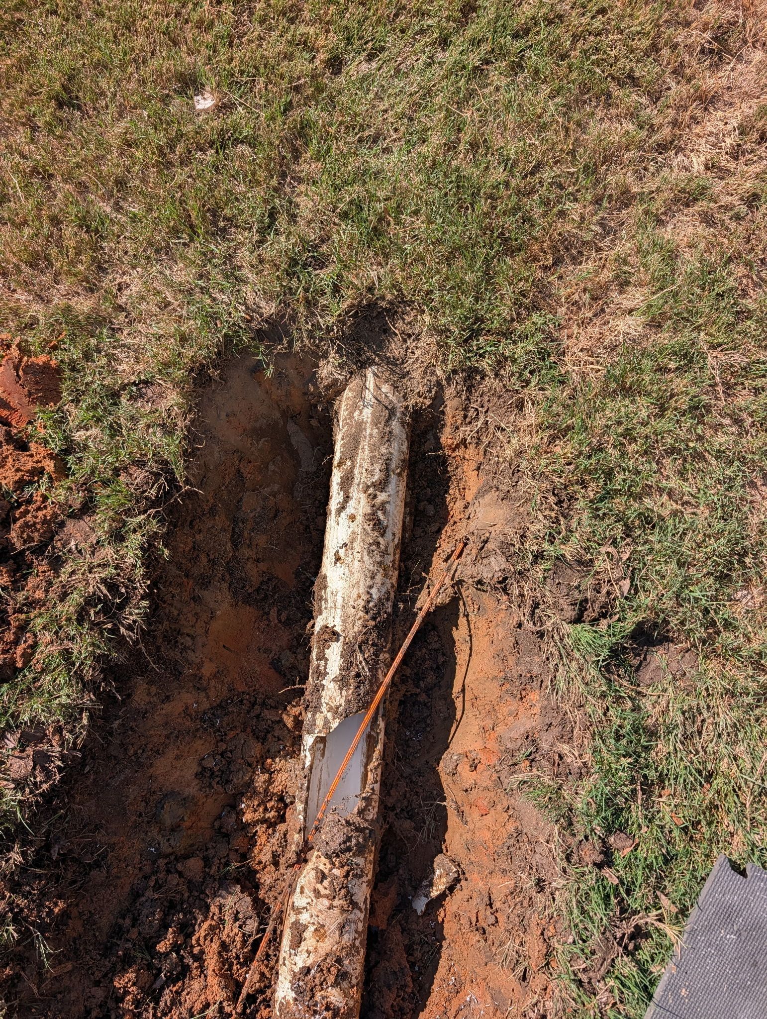 A narrow erosion channel cuts through dry grass and reddish soil, with exposed roots or rock in the center.