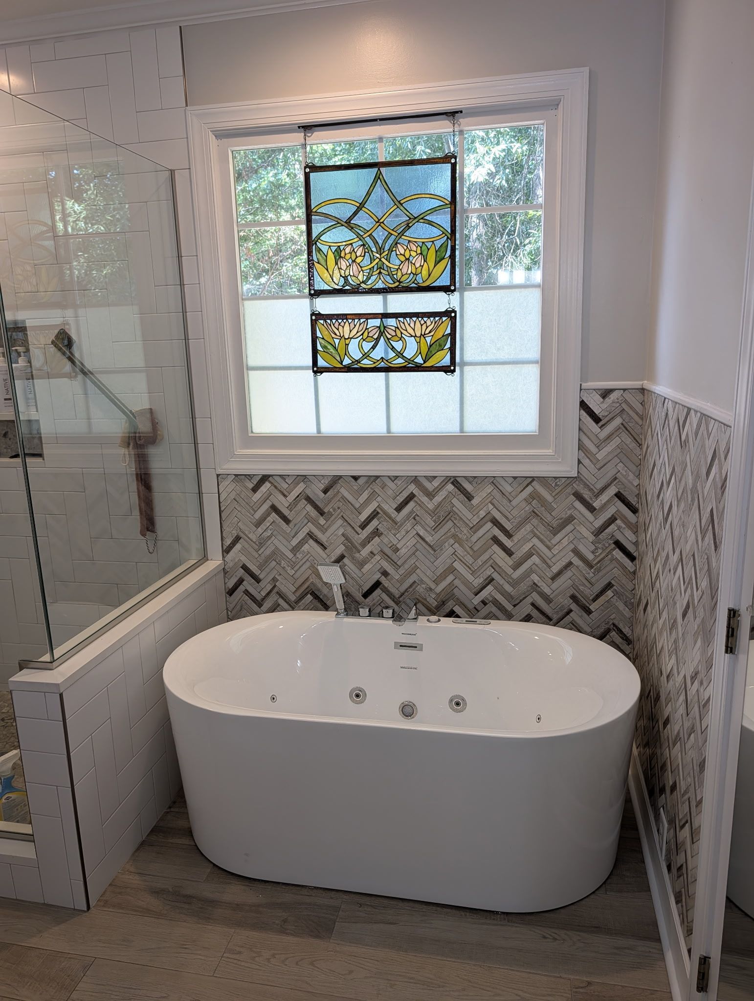 Modern bathroom with freestanding tub, herringbone tile, glass shower, and stained-glass window above the tub