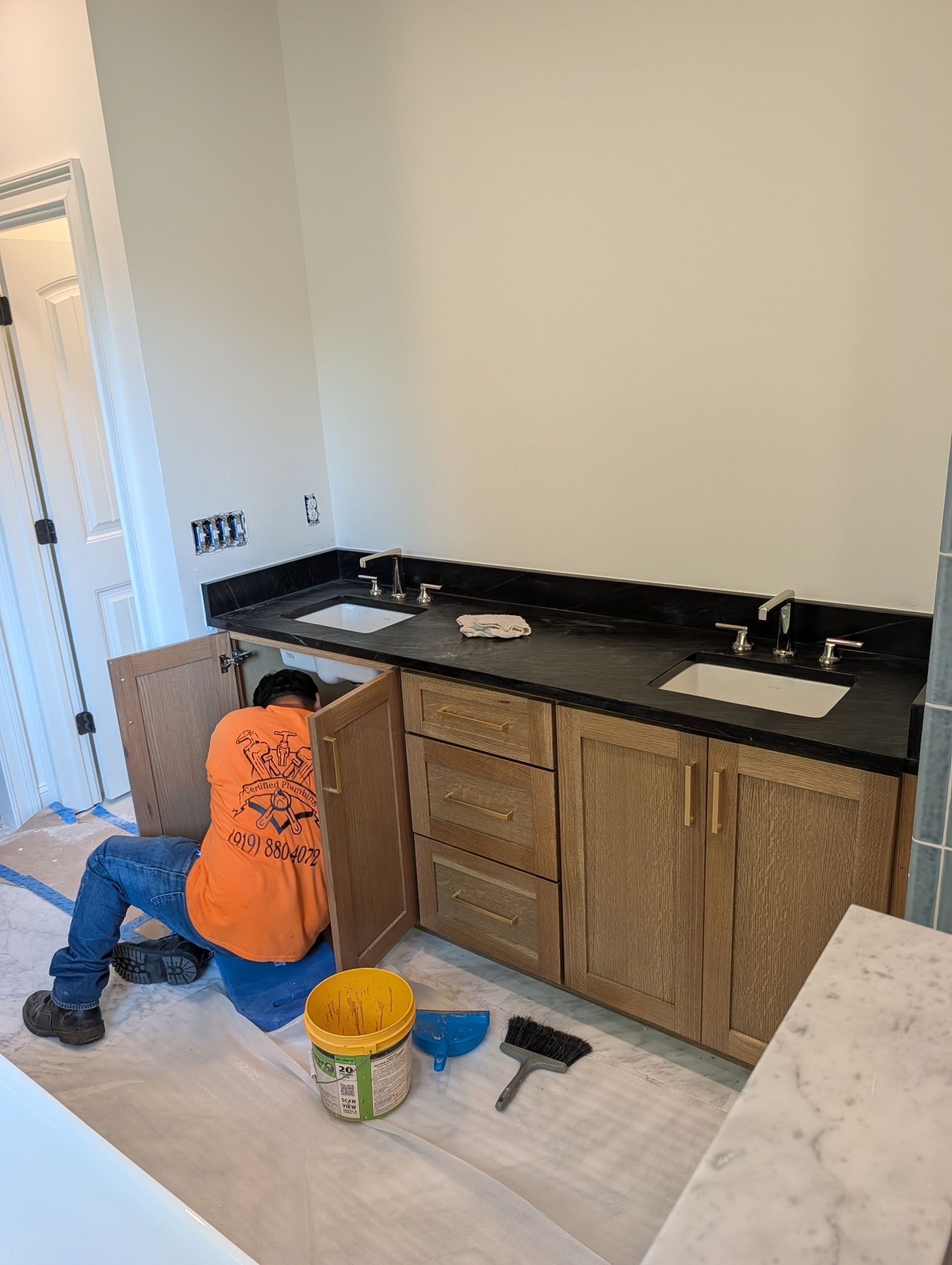 Person kneeling beside wood cabinets, installing a dark countertop in a kitchen under renovation.