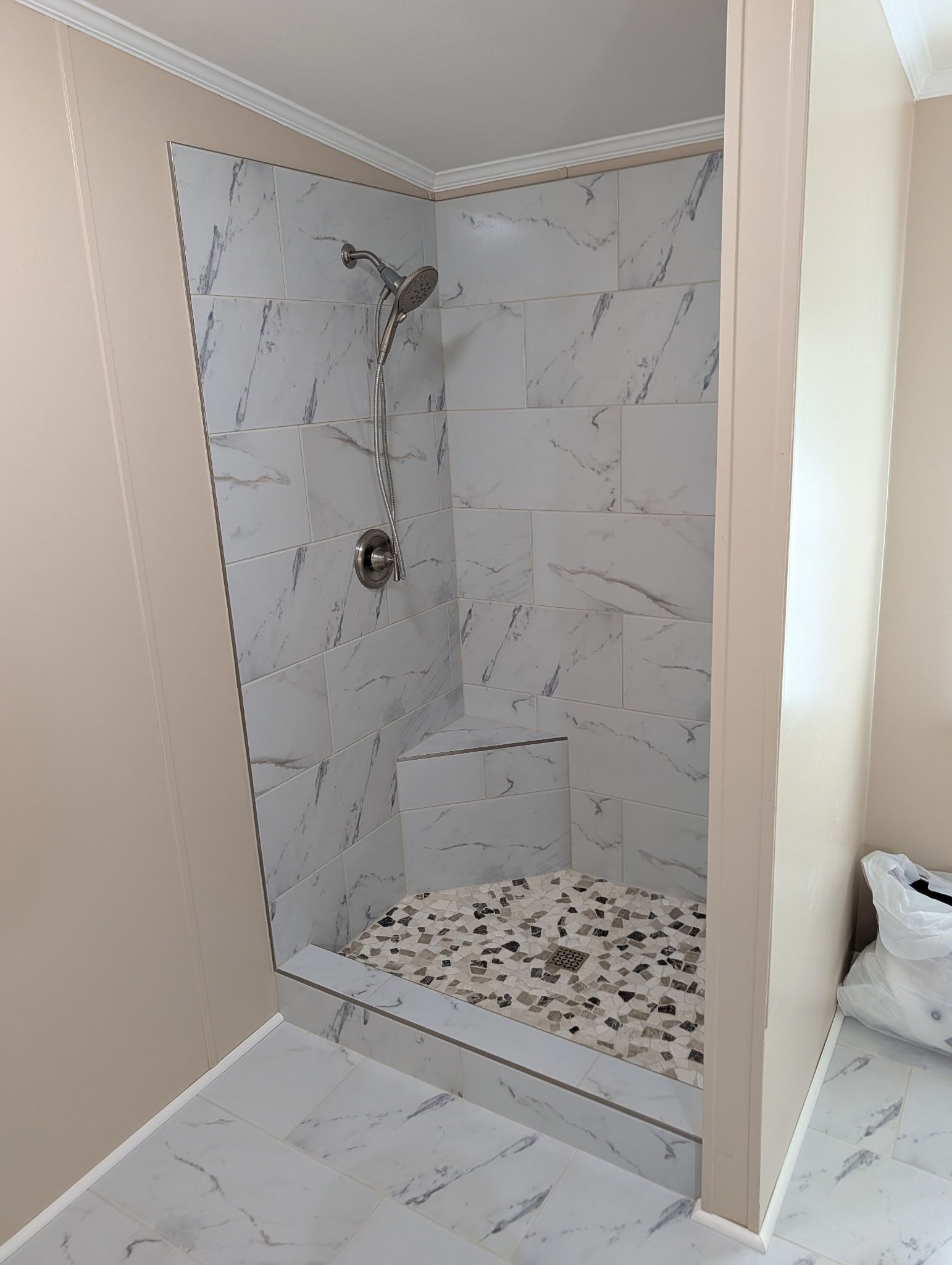 Marble-tiled walk-in shower with glass opening and pebble floor drain in a bathroom