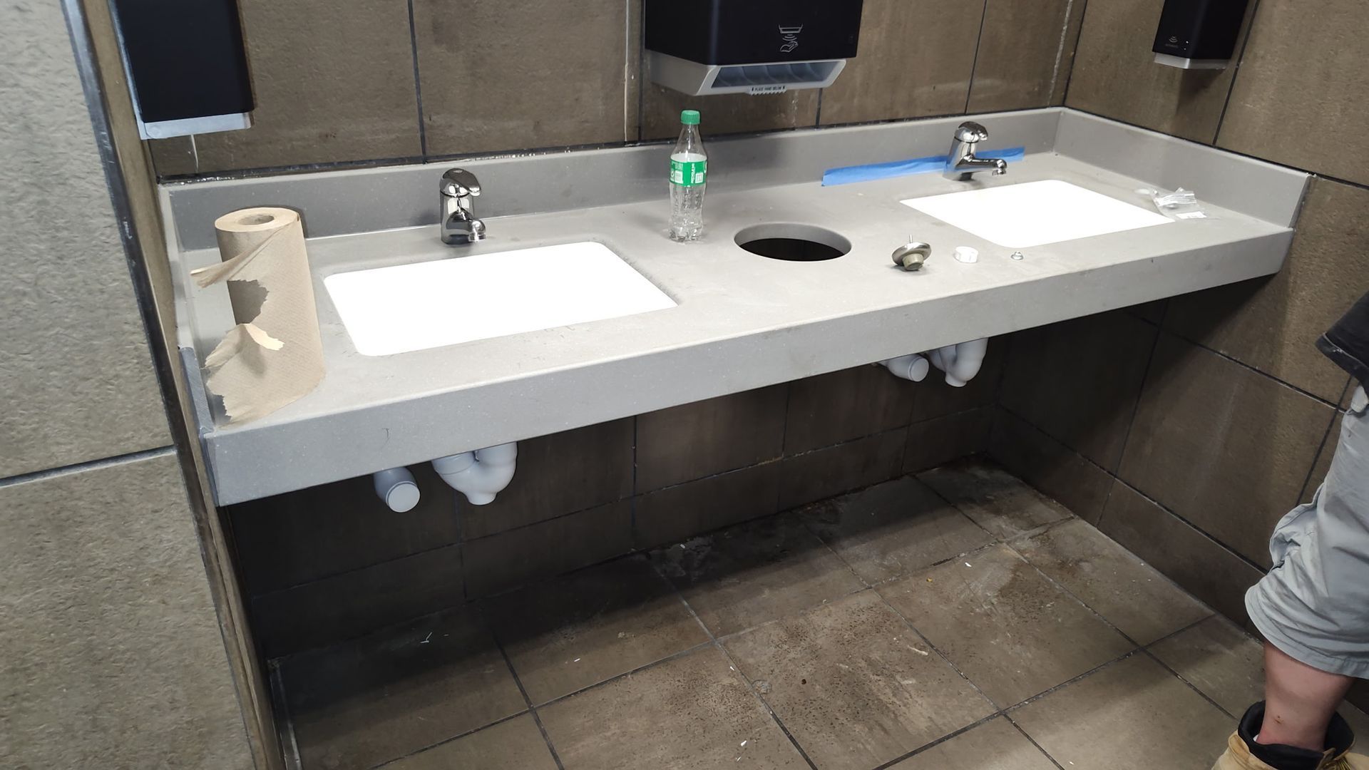 Two bathroom sinks with silver faucets installed in a grey counter against tiled walls, with a partial view of a person.