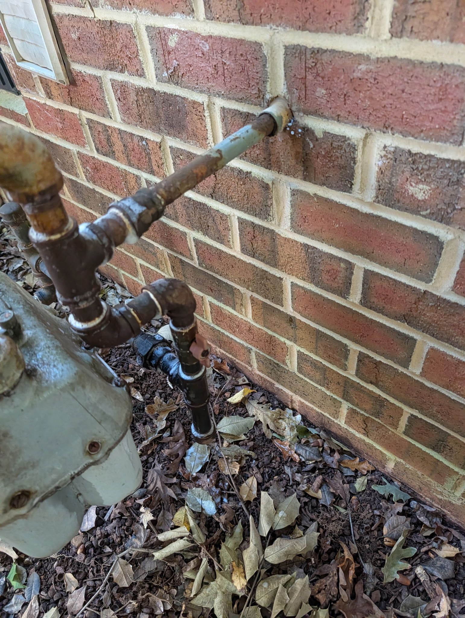 A gas meter with rusty pipe connections attached to a brick wall exterior.