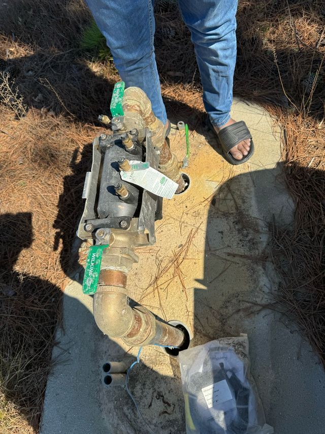 Person near a water meter, standing over the utility, wearing jeans and sandals.