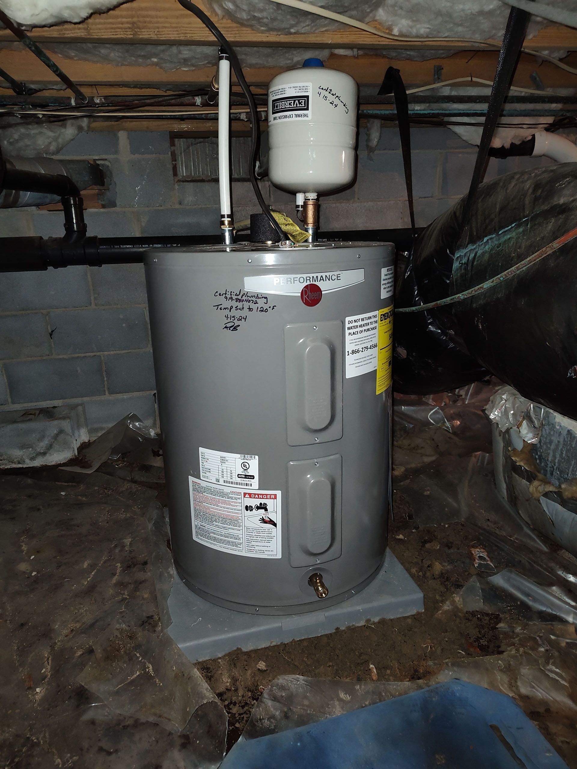 A gray water heater with a white expansion tank in a dimly lit crawlspace.