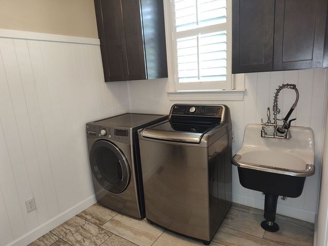 Laundry room with washer, dryer, sink, and cabinets; white walls with wood paneling.