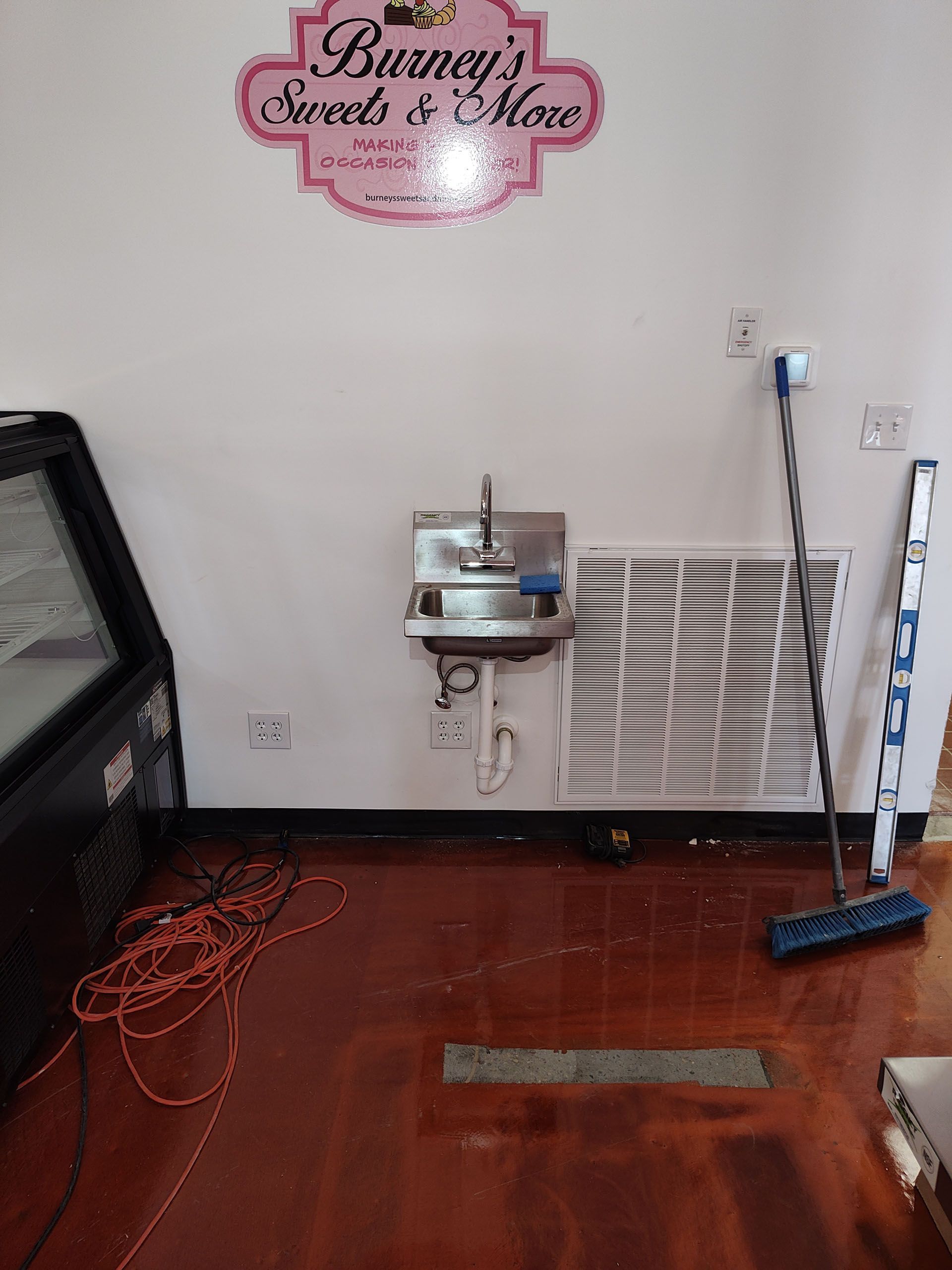 Interior shop space with a sink, air vent, broom, and exposed wiring on the floor. 