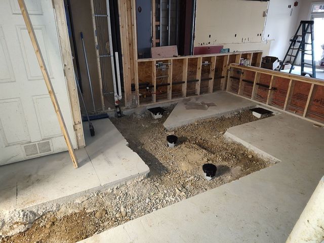 Interior view of a construction site with exposed plumbing and concrete work in a room with framed walls.