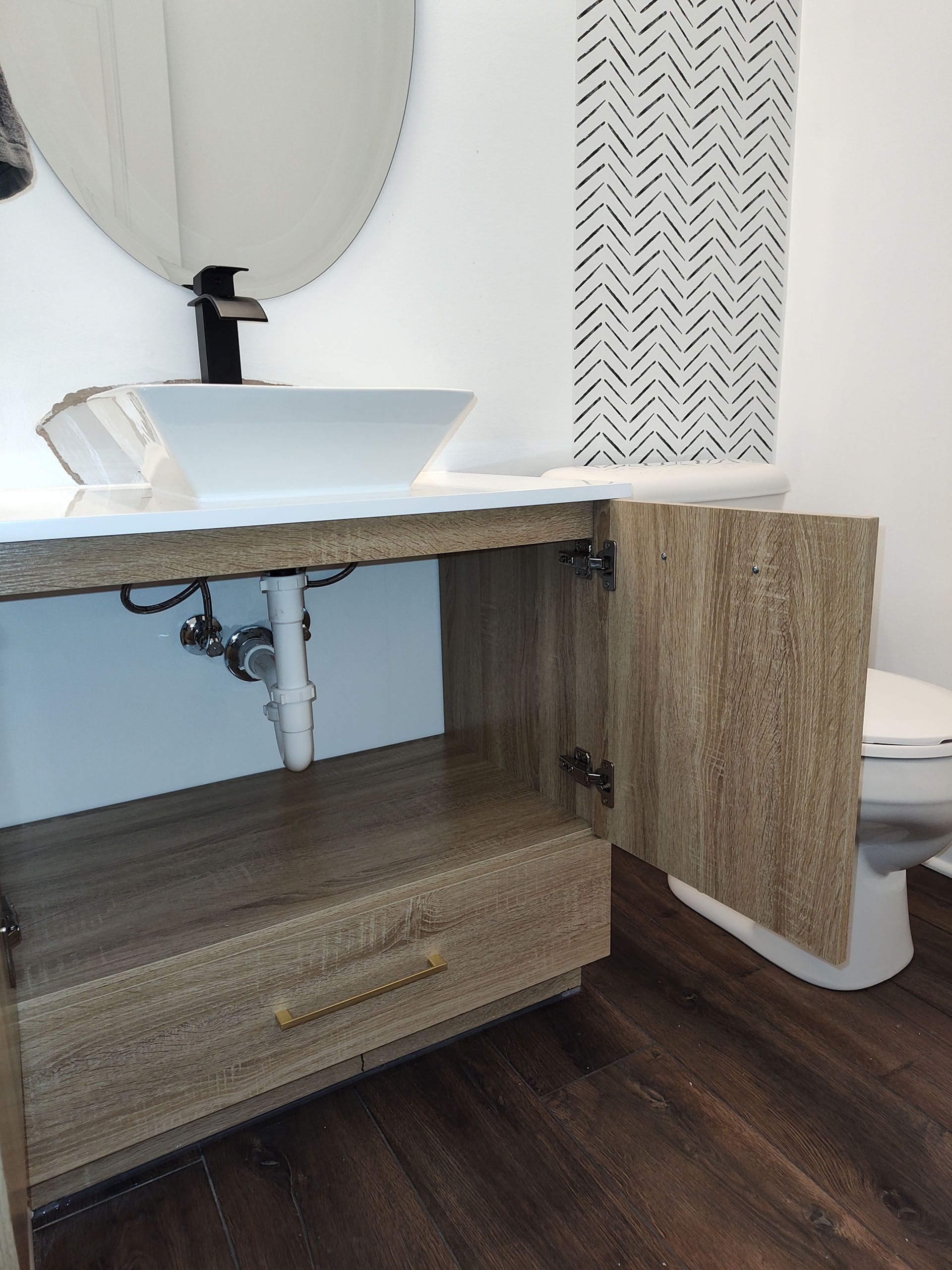 Bathroom vanity with open cabinet door, white sink, black faucet, and patterned shower curtain.
