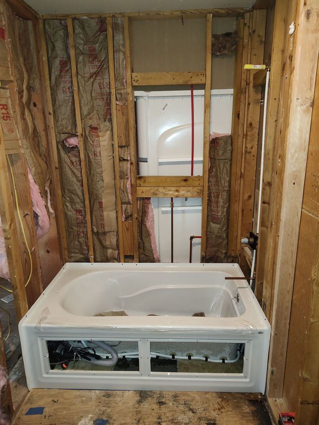 A bathtub is installed in a bathroom under construction, surrounded by wooden framing and insulation.