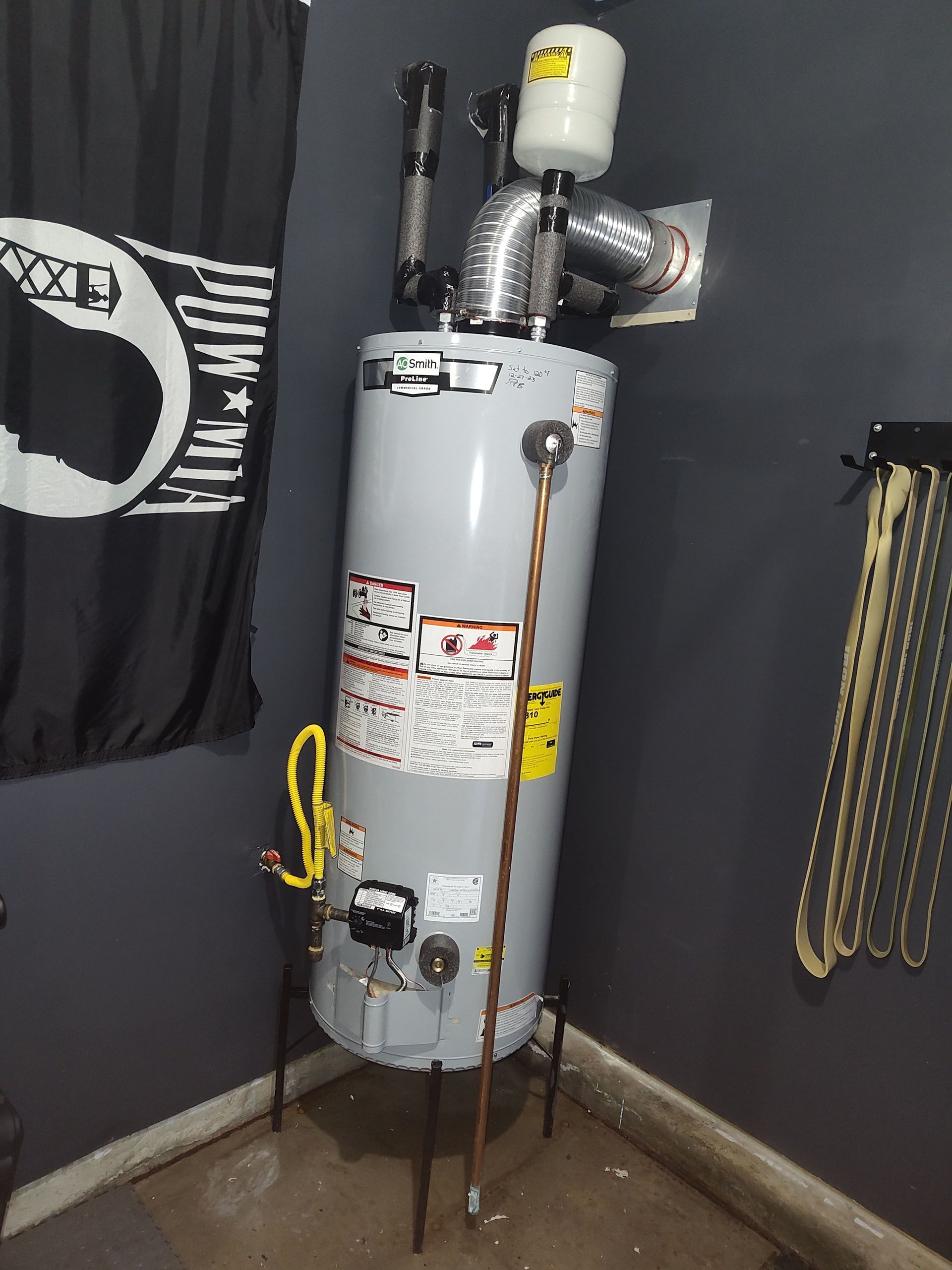 Gray water heater in corner with exhaust pipes and a flag.