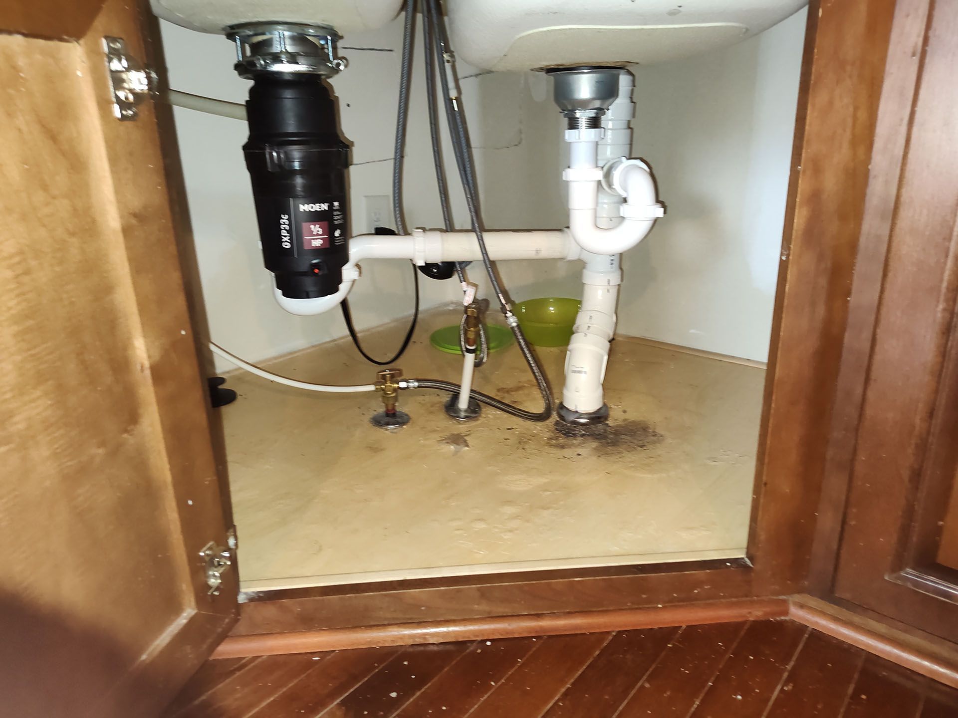 Kitchen sink cabinet interior with garbage disposal and drain pipes; water stains on the bottom.