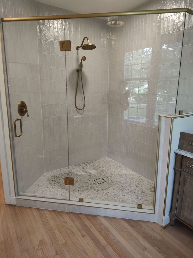 Corner shower with glass doors, brass fixtures, and pebble tile floor.