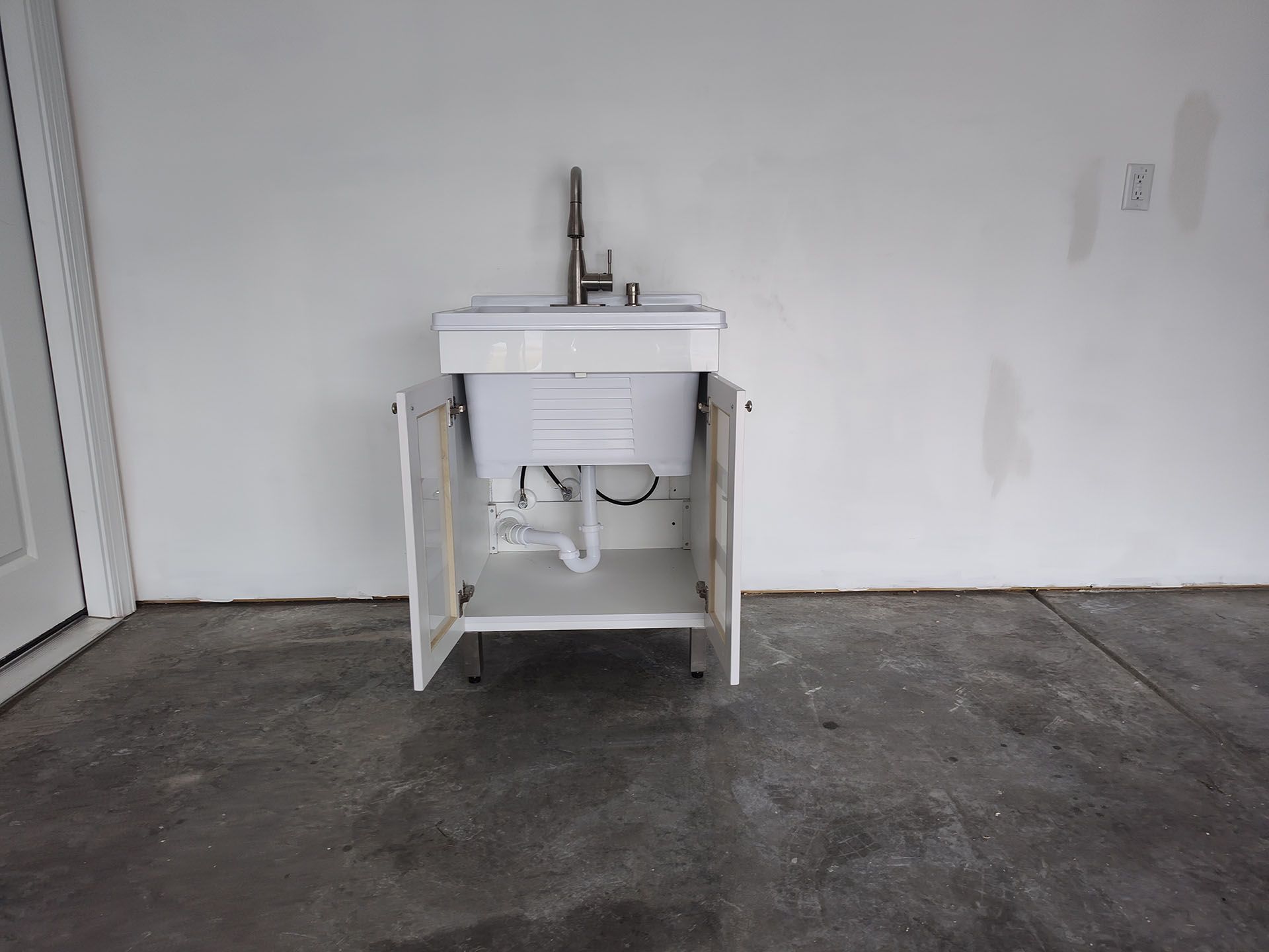 White utility sink and cabinet against a white wall in a garage.