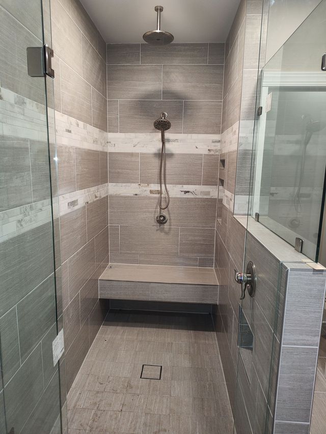 Modern shower with glass doors, tiled walls in gray and white, and a built-in bench.