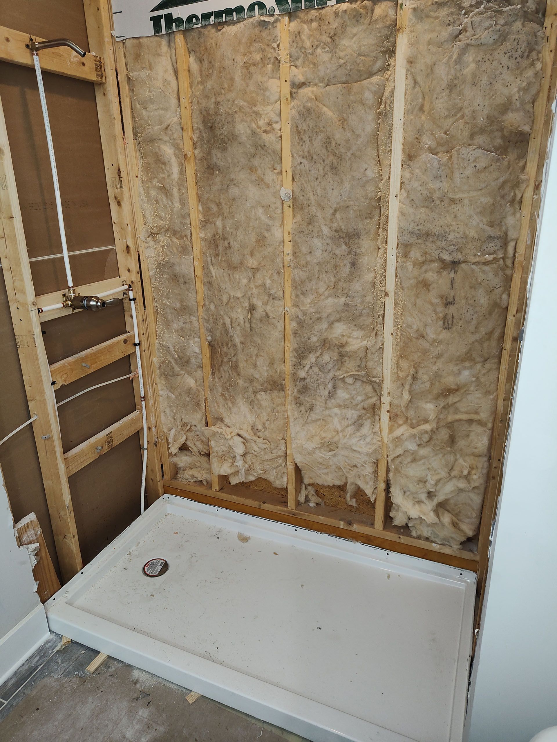 Framed shower stall under construction; insulation between studs, white shower base installed.
