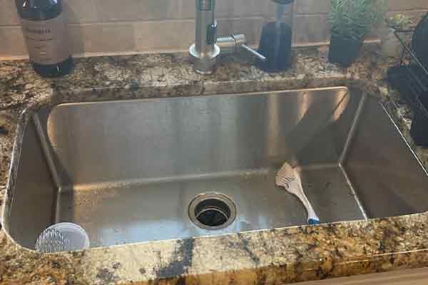 Stainless steel kitchen sink with a brush inside, set in a granite countertop.