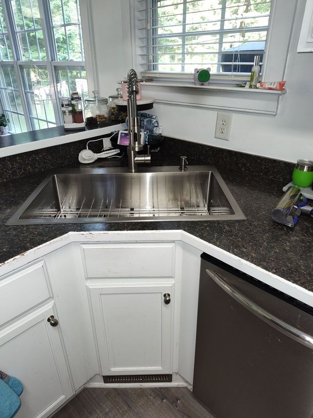 Stainless steel kitchen sink in a corner, with cabinets below and a window in the background.