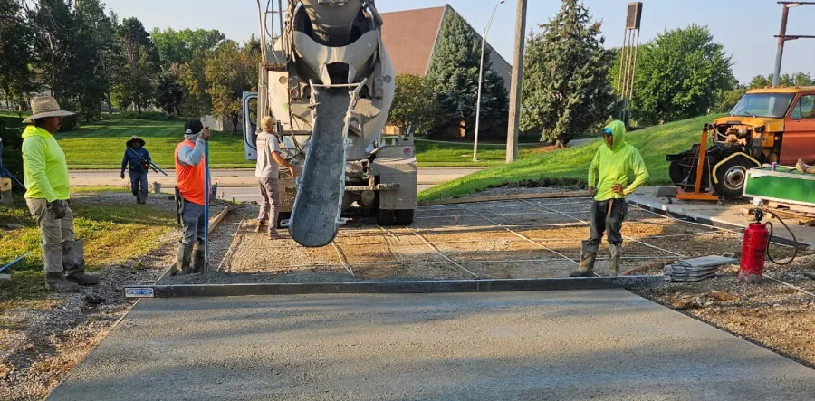 Workers pouring concrete from a cement truck onto a prepared surface outdoors.