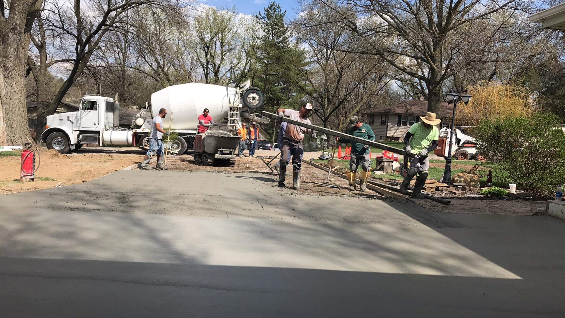 Concrete truck pouring cement on driveway, construction workers using tools. Outdoors on a sunny day.