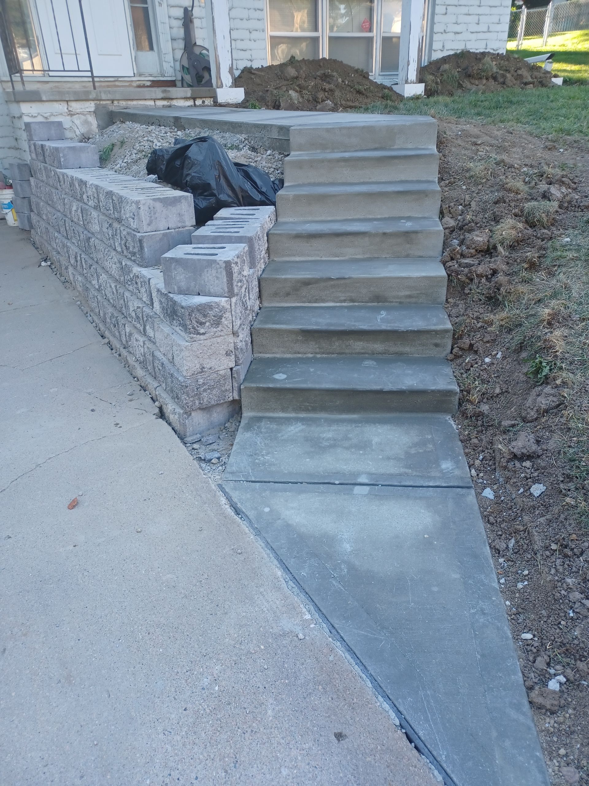 Concrete steps and retaining wall under construction next to a sloped concrete path.